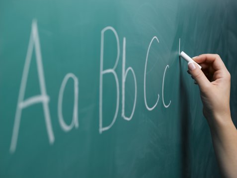 Woman writing alphabet on chalkboard, close-up